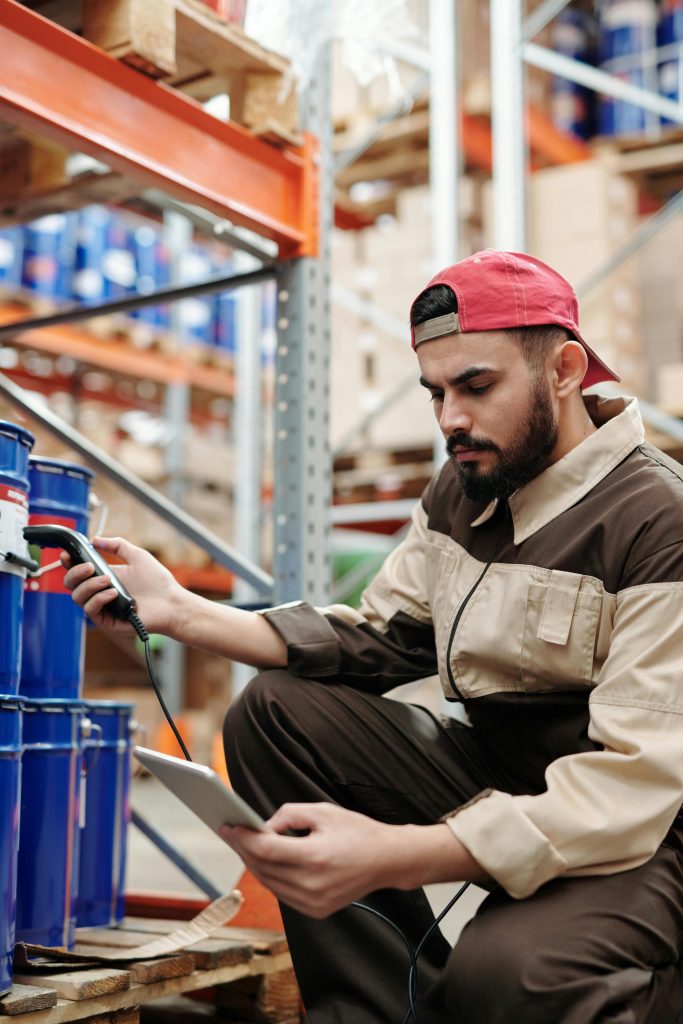 Man in warehouse scanning items with digital tablet, focused on inventory management.